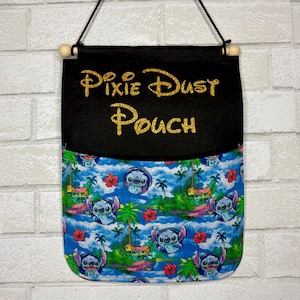 May include: A hanging fabric pouch featuring a black top section with the gold glitter text Pixie Dust Pouch and a bottom pocket section with a blue tropical pattern of palm trees, red hibiscus flowers, and the blue character Stitch.