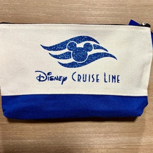 May include: A white and blue canvas zippered pouch with the Disney Cruise Line logo and Mickey Mouse head. The logo is in blue glitter.
