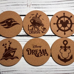 May include: Six round cork coasters with brown designs. The designs include a Mickey Mouse silhouette, a cruise ship with the text "Let's Cruise", a ship's wheel with a Mickey Mouse silhouette, a cruise ship, the word "Disney Dream", and an anchor with a Mickey Mouse silhouette.