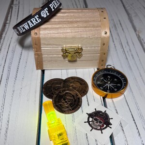 May include: A pirate-themed collection featuring a wooden treasure chest, a black wristband with "BEWARE OF PIRATES" text, a compass, coins, a yellow light, and a skull and crossbones tattoo.