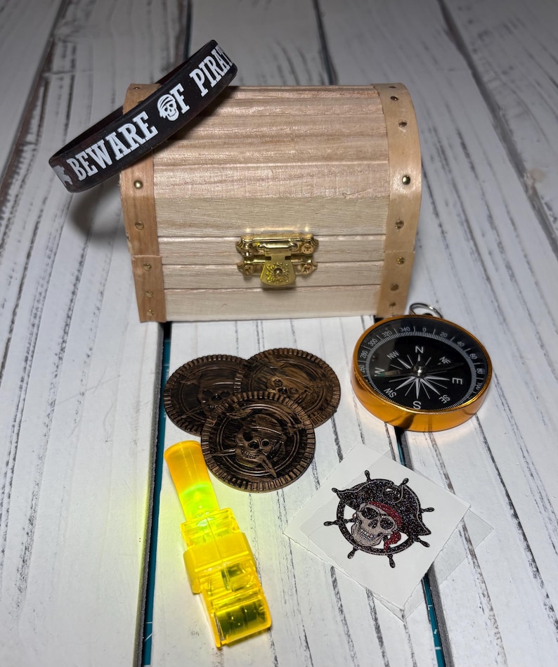 May include: A pirate-themed collection featuring a wooden treasure chest, a black wristband with "BEWARE OF PIRATES" text, a compass, coins, a yellow light, and a skull and crossbones tattoo.