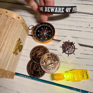 May include: A pirate-themed collection featuring a treasure chest, compass, coins, and a rubber bracelet that reads "BEWARE OF PIRATES". Includes a temporary tattoo and a small, yellow, glowing light.