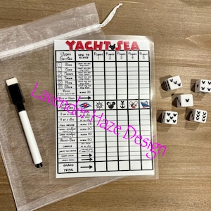 May include: A white game board with the title "Yacht Sea" and a scorecard for a dice game. The board has a section for upper scores, lower scores, and a grand total. There are five columns for players. The board is on a wooden surface with five white dice with black Mickey Mouse ears on each side.