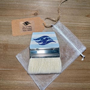 May include: A paint brush with a light blue and white striped design and a silver metal handle. The brush has a white bristle head and is packaged with a small tag and a sheer white bag. The tag reads "You've been Pixie Dusted! From: 00000".