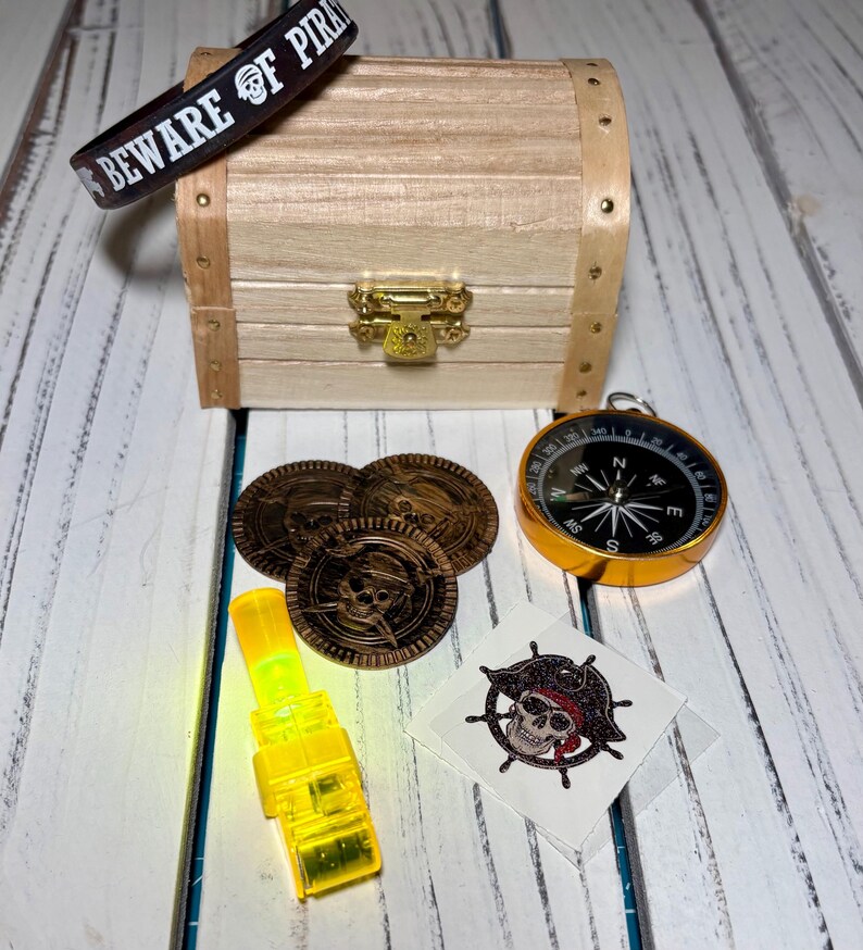 May include: A pirate-themed collection featuring a wooden treasure chest, gold coins, a compass, a glow stick, a temporary tattoo, and a bracelet with the text "BEWARE OF PIRATES".