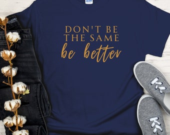May include: Navy blue t-shirt with the text "Don't be the same be better" in gold lettering.
