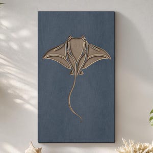 Op de afbeelding: Een houten wandkunstwerk met een gelaagd ontwerp van een pijlstaartrog. Het kunstwerk is gemonteerd op een rechthoekige, donkerblauwe achtergrond. De pijlstaartrog is lichtbruin van kleur met een lange, gebogen staart. De kunst wordt tentoongesteld in een woonkamer met kustthema.