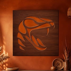 Op de afbeelding: Een houten wandkunstwerk met een gestileerd oranje slangenkopontwerp tegen een donkerbruine achtergrond. Het kunstwerk wordt getoond in een kamer met een warm, aards kleurenpalet, inclusief een houten kast en decoratieve planten.