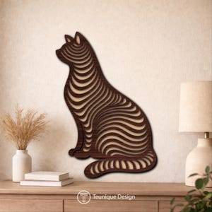 Op de afbeelding: Een houten katten silhouet met een gelaagd ontwerp, met afwisselend donkerbruine en lichtbeige tinten. De kat zit, met de tekst "Teunique Design" onderaan. Dit decoratieve stuk is geschikt voor interieurdecoratie.