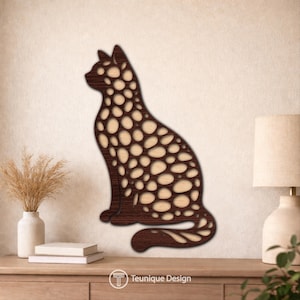 Op de afbeelding: Houten katten silhouet met een uniek ontwerp. De kat is donkerbruin met een patroon van lichtbruine ovale uitsparingen. De kat zit rechtop. De afbeelding bevat de tekst "Teunique Design".