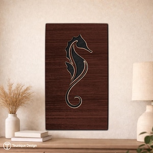 Puede incluir: Arte de pared de madera con un diseño de caballito de mar. El caballito de mar es negro con detalles dorados, sobre un fondo de vetas de madera marrón oscuro. La obra de arte rectangular está montada en la pared.