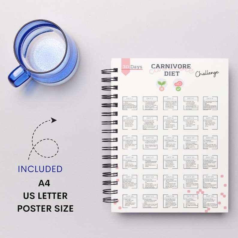 May include: A white spiral bound notebook with a 30-day Carnivore Diet Challenge on the cover. The cover has a pink and white design with a small illustration of a plant and a piece of meat. The notebook is on a gray surface.