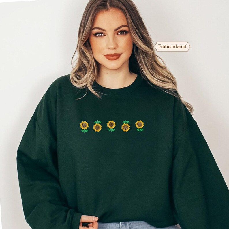 A woman wearing a green sweater with a row of yellow sunflowers embroidered on it.