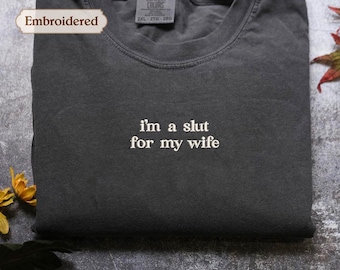 May include: A charcoal gray crew neck t-shirt featuring white embroidered text on the chest that reads, i'm a slut for my wife. The garment includes a Comfort Colors brand label at the inner neckline, which also displays the size 2XL 2TG 2EG.