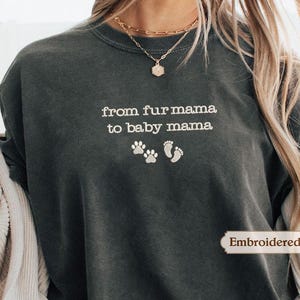 A person wearing a gray sweatshirt with the text "from fur mama to baby mama" printed on it, along with paw prints and a small heart symbol.