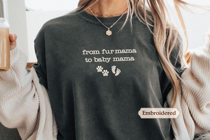 A person wearing a gray sweatshirt with the text "from fur mama to baby mama" printed on it, along with paw prints and a small heart symbol.