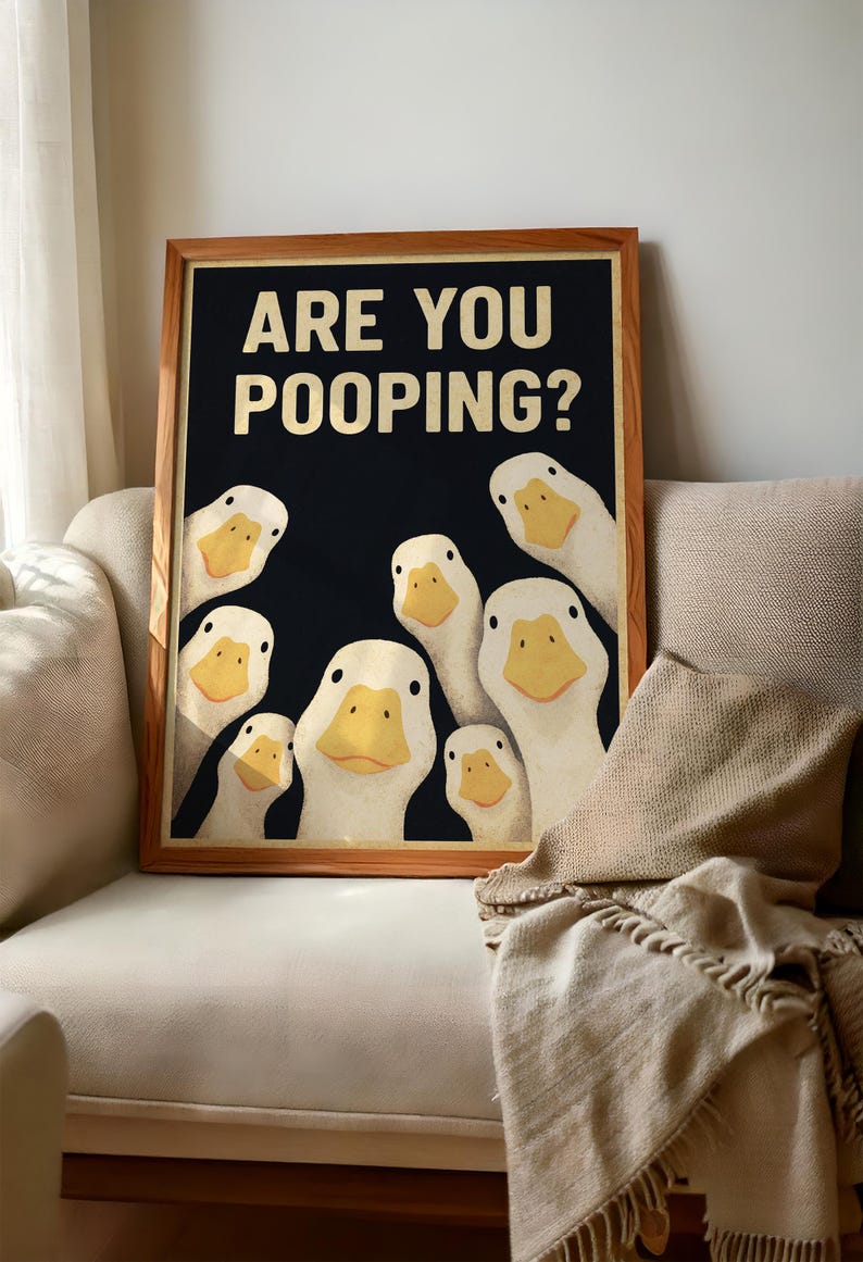 A framed poster with a humorous cartoon duck illustration and the text "ARE YOU POoping?" displayed on a couch.