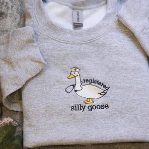 A gray sweatshirt with a cartoon image of a duck wearing a nurse's hat and the text "registered silly goose" printed on it.