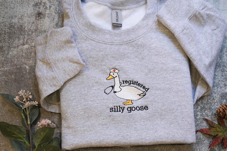 A gray sweatshirt with a cartoon image of a duck wearing a nurse's hat and the text "registered silly goose" printed on it.
