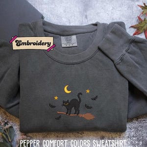 A gray sweatshirt with a black cat embroidered on it, along with a label that says "Embroidery" and a small leaf decoration.