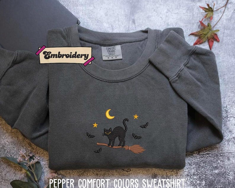 A gray sweatshirt with a black cat embroidered on it, along with a label that says "Embroidery" and a small leaf decoration.