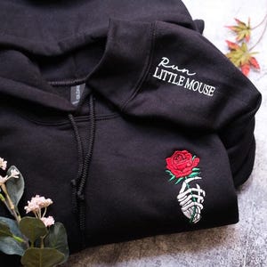 a black hoodie with a rose embroidered on it