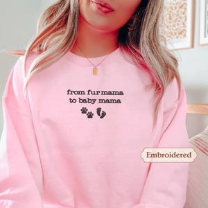 A woman wearing a pink sweatshirt with the text "from fur mama to baby mama" and paw prints on it.