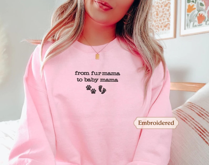 A woman wearing a pink sweatshirt with the text "from fur mama to baby mama" and paw prints on it.