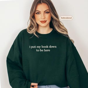 A woman wearing a green sweatshirt with the text "I put my book down to be here" printed on it.