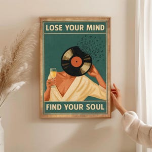 May include: A framed poster with the text "LOSE YOUR MIND FIND YOUR SOUL". The artwork features a person with a vinyl record in place of a head, holding a glass of wine. Musical notes emanate from the record. The poster has a teal background.