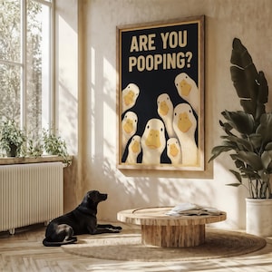 A black dog is sitting on the floor in a room with a large poster of ducks above it, and a potted plant to the right.