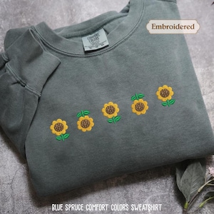 a gray sweatshirt with a row of yellow sunflowers embroidered on it, along with a label indicating that it is an embroidered item.