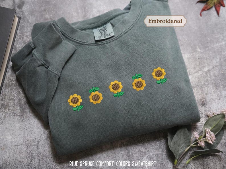 a gray sweatshirt with a row of yellow sunflowers embroidered on it, along with a label indicating that it is an embroidered item.