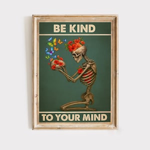 May include: A framed poster with the text "BE KIND TO YOUR MIND". The artwork features a skeleton kneeling, holding flowers and butterflies. The skeleton's head is adorned with red flowers, and colorful butterflies are depicted around it.