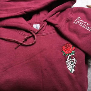 a red hoodie with a rose embroidered on it