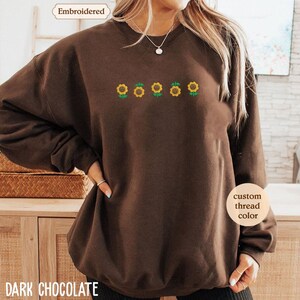 A woman wearing a brown sweater with a design of four sunflowers embroidered on it.