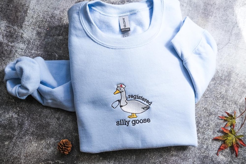 A light blue sweatshirt with a cartoon goose wearing a nurse's hat and the text "registered silly goose" printed on it.