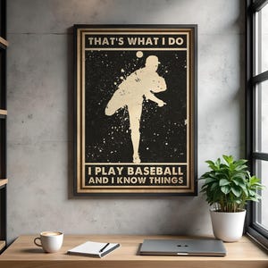 Op de afbeelding: Ingelijste honkbalposter met een zwarte achtergrond en een silhouet van een honkbalspeler die gooit. De tekst luidt "THAT'S WHAT I DO, I PLAY BASEBALL AND I KNOW THINGS" in goud.
