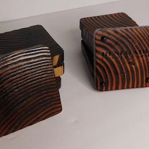 Könnte beinhalten: Satz mit vier Untersetzern aus Holz mit einem welligen Holzmaserungsmuster. Die Untersetzer sind schwarz und braun mit dem Text "Renegade Flower Farm" auf dem unteren Untersetzer.