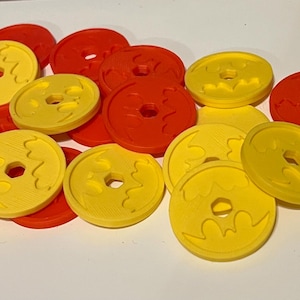 May include: A collection of yellow and red plastic game pieces with a bat design. The pieces are round and have a hole in the center.