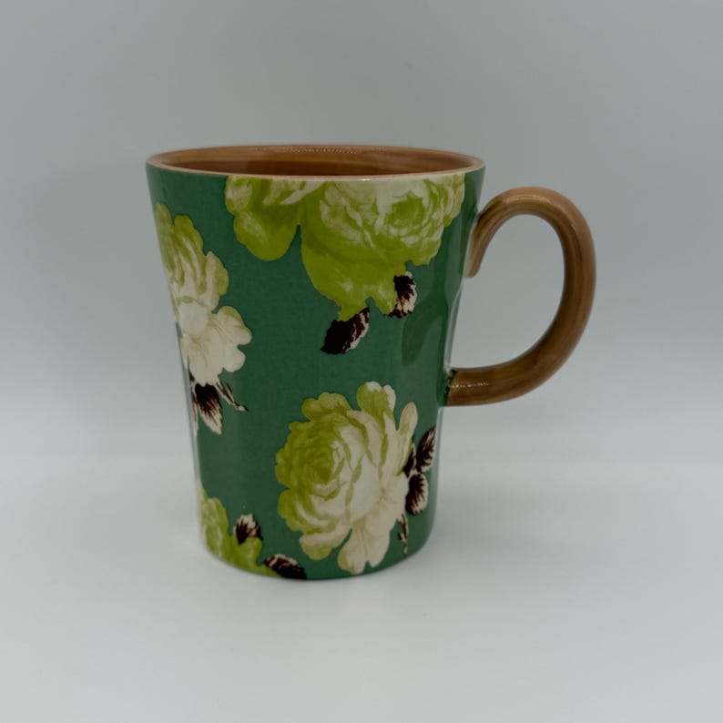 Puede incluir: Taza de cer&aacute;mica con un dise&ntilde;o floral de rosas blancas y verdes sobre fondo verde. El interior y el asa son marrones. Ideal para bebidas calientes, con una capacidad aproximada de 350 ml.