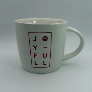 May include: White ceramic mug with a curved handle. The mug features the word "JOYFUL" in red block letters inside a red rectangular frame. A peace symbol replaces the "O".