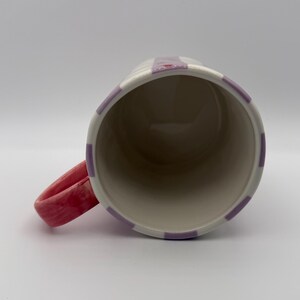 Pu&ograve; includere: Una tazza in ceramica con base bianca, ornata da strisce verticali lavanda. Il manico &egrave; di un vivace colore rosso-rosa. L'interno della tazza &egrave; beige neutro, offrendo un netto contrasto con il design esterno. Un pezzo semplice ma elegante.