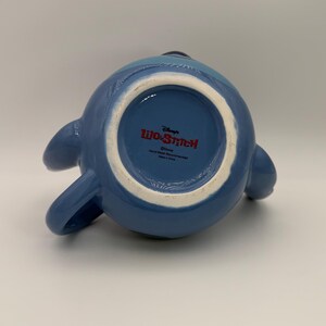Puede incluir: Una taza de cer&aacute;mica azul con la forma del personaje Stitch de Lilo & Stitch de Disney. La taza tiene un asa y dos ap&eacute;ndices laterales. La parte inferior de la taza presenta el logotipo de Lilo & Stitch y el texto "Hand Wash Recommended".