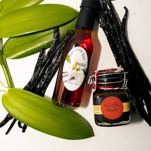 May include: An overhead shot of vanilla products, including a bottle of Pure Vanilla Extract and a jar of Vanilla Paste. The extract bottle is labeled with "Made with Love." Also shown are vanilla beans and green leaves.