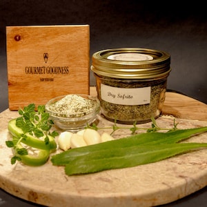 May include: A jar of Dry Sofrito spice mix with a gold lid, a small bowl of the spice, and fresh ingredients on a wooden cutting board. The wooden box in the background has the text "GOURMET GOODNESS".