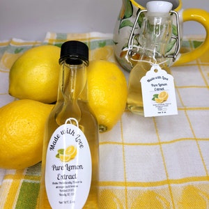 May include: Two small glass bottles of pure lemon extract, one with a white label that says "Made with Love Pure Lemon Extract" and the other with a white label that says "Made with Love Pure Lemon Extract Shake Periodically Flavor is stronger the older it gets Bottled 2021 Brody 12/22 Net WT. 5 oz.". The bottles are sitting on a yellow and white checkered tablecloth with lemons around them.