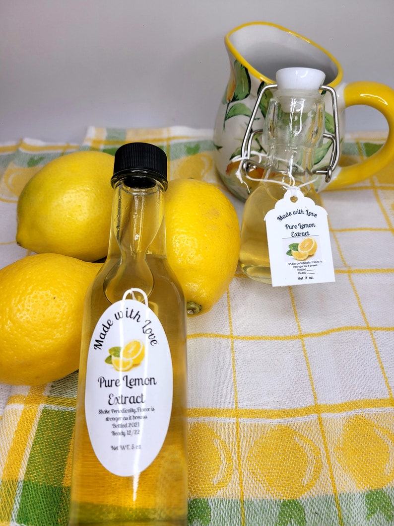 May include: Two small glass bottles of pure lemon extract, one with a white label that says "Made with Love Pure Lemon Extract" and the other with a white label that says "Made with Love Pure Lemon Extract Shake Periodically Flavor is stronger the older it gets Bottled 2021 Brody 12/22 Net WT. 5 oz.". The bottles are sitting on a yellow and white checkered tablecloth with lemons around them.
