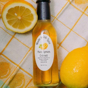 May include: A glass bottle of pure lemon extract with a white label that reads "Made with Love, Pure Lemon Extract, Shake Periodically, Flavor is stronger cold, Bottled 2022, Best By 04/23, Net Wt. 5 oz". The bottle is sitting on a yellow and white checkered cloth with a lemon slice and a whole lemon.