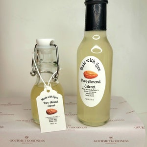 May include: Two glass bottles of pure almond extract, both with a white label that says "Made with Love" and "Pure Almond Extract". The larger bottle is 2 oz and the smaller bottle is 1 oz. Both bottles are on a white background with a repeating pattern of "Gourmet Goodness Made with Love".